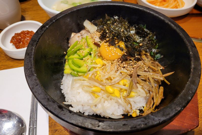 Koreańskie danie dolsot bibimbap podane w kamiennej misie, poza tym na stole przystawki