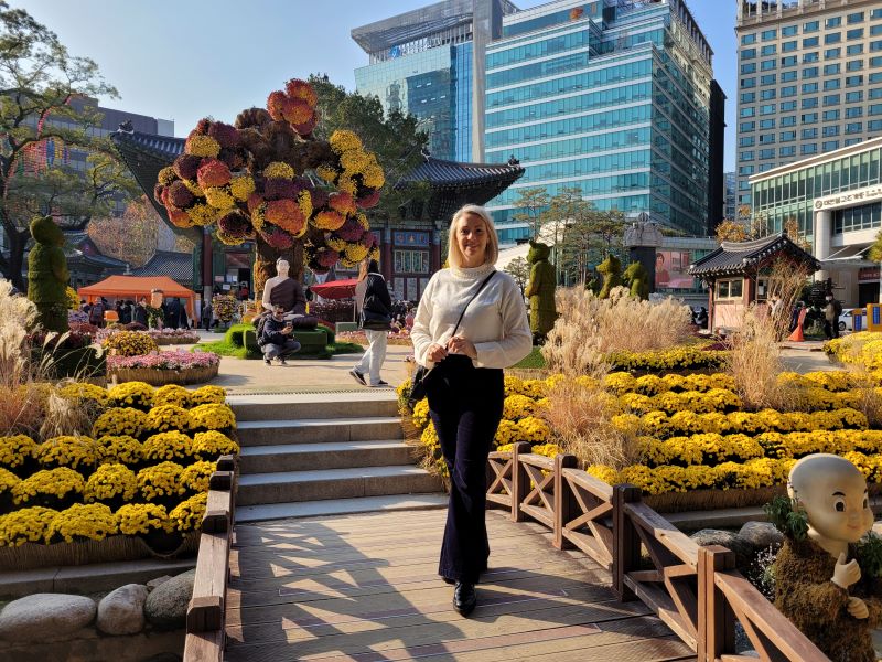 Dr K. Juszczyk-Frelkiewicz, prof. UŚ stoi w parku świątyni buddyjskiej w Seulu, w tle widać wieżowce stolicy