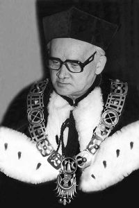 starszy mężczyzna w okularach ubrany w togę z ozdobnym futrzanym kołnierzem i łańcuchem dziekańskim na szyi