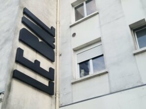 zdjęcie przedstawiające szarą ścianę z dwoma oknami po prawej, po lewej stronie czarny napis LE BAL