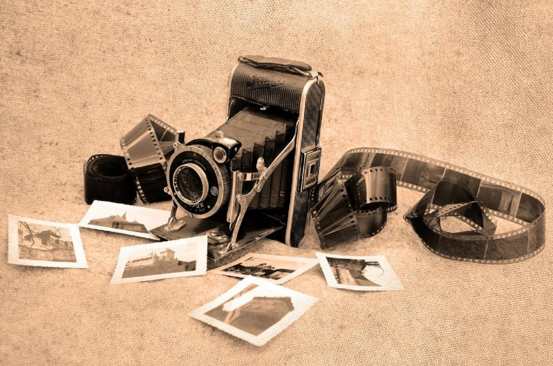 zdjęcie przedstawiające aparat fotograficzny starego typu z wyciągniętą kliszą oraz leżącymi zdjęciami