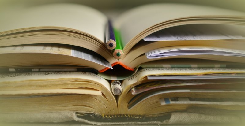 zdjęcie przedstawiające otwartą szeroko książkę z zakładkami - złożonymi kartkami papieru, na środku książki leża dwie kolorowe kredki