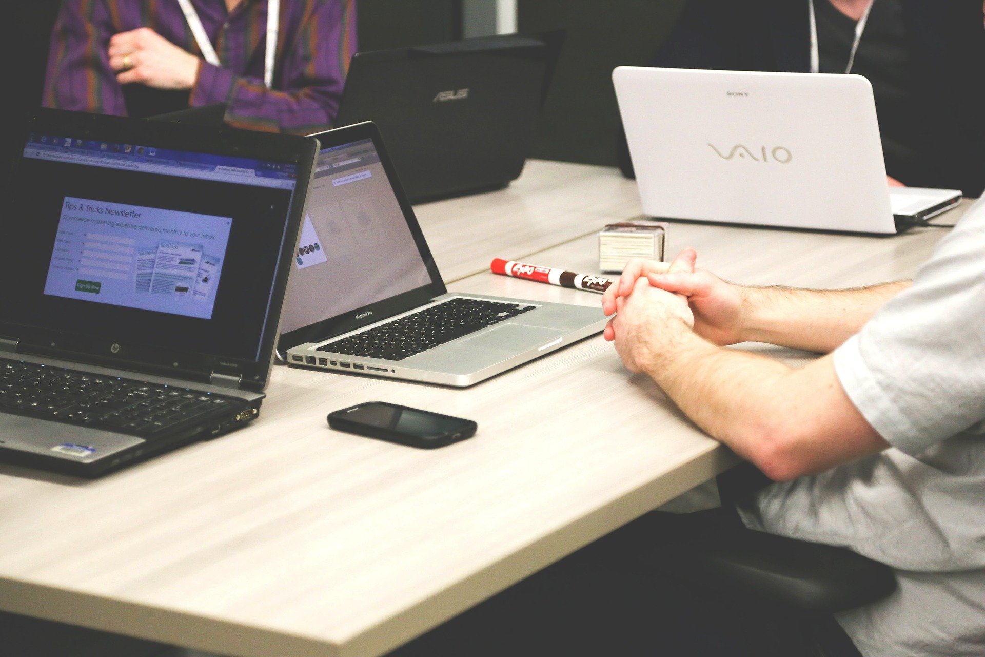 Na stole 3 laptopy na drewnianym biurku, oparte ręce mężczyzny