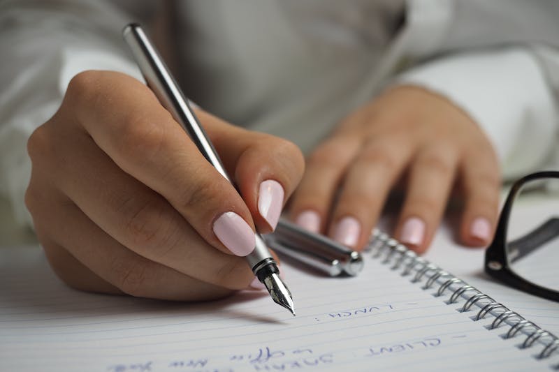 Kobieta w białej koszuli z długimi rękawami trzyma pióro, pisze na papierze