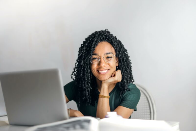 Uśmiechnięta młoda kobieta siedząca przed laptopem