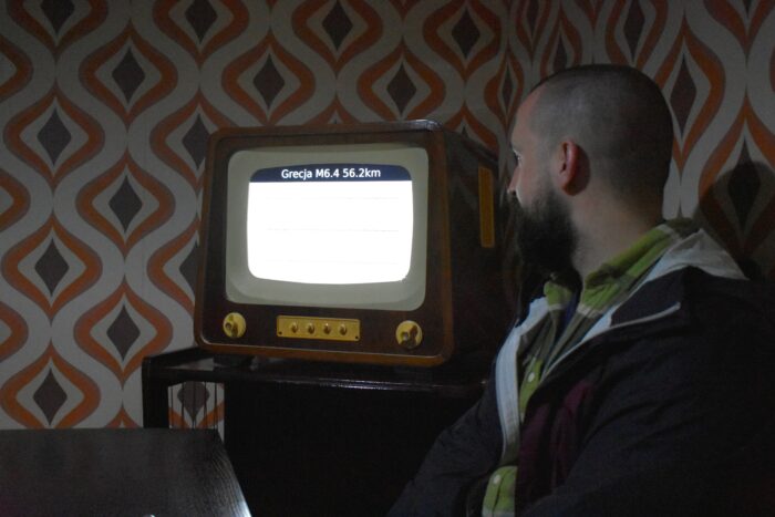 A man looking at the old-fashioned television set behind him. Mężczyzna obrócony do stojącego za nim staromodnego telewizora.