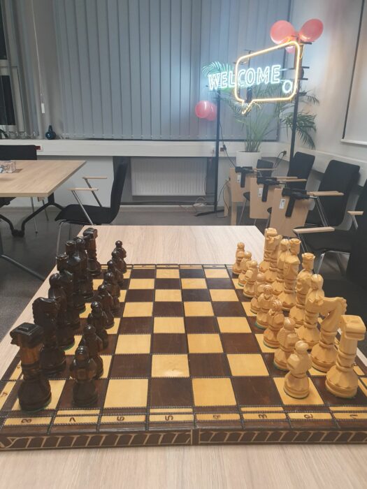 A board with chess ready to play with Welcome Point neon in the background. Plansza z szachami gotowa do rozgrywki, w tle neon Welcome Point.