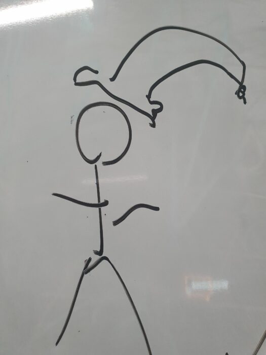 A marker drawing of a stick figure in a cap or hat. Rysunek osoby w kapeluszu wykoknany markerem na białe tablicy.