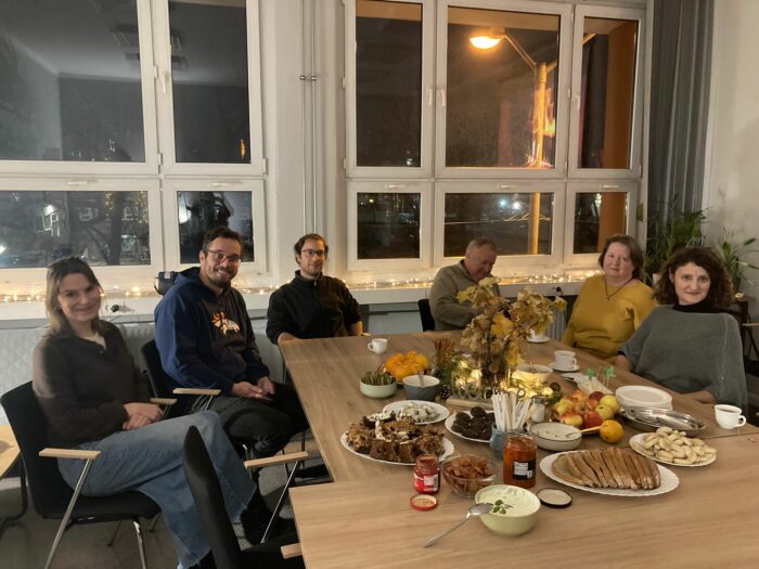 A group of six people sitting at the table and smiling to the camera. Grupa sześciu osób siedzących przy zastawionym stole i uśmiechających się do zdjęcia.