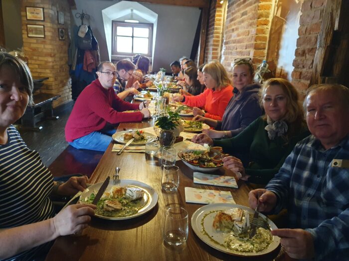 Group of outdoor game participants at the dinner table. Grupa uczestników gry terenowej siedząca przy stole przy obiedzie.
