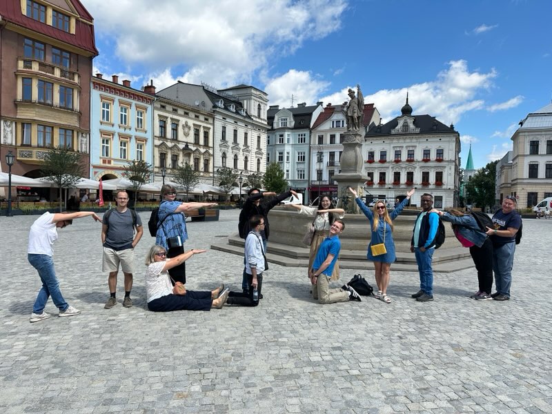 A group of people in the town square with their bodies positioned as the Cieszyn inscription. Grupa ludzi na rynku miasta stojących w pozycjach, z których układa się napis "Cieszyn"