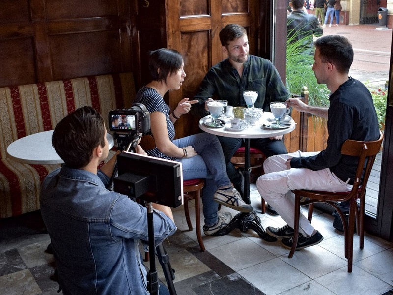 A man with a camera records three people in the cafe / Mężczyzna nagrywa za pomocą kamery trzy osoby siedzące przy stoliku w kawiarni