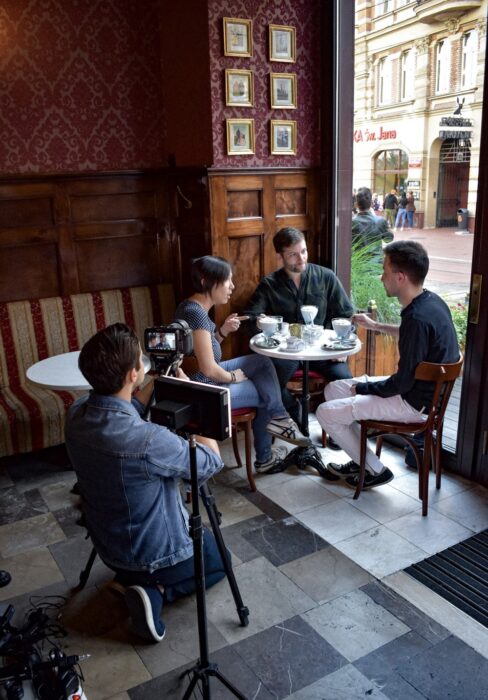 A man with a camera records three people in the cafe / Mężczyzna nagrywa za pomocą kamery trzy osoby siedzące przy stoliku w kawiarni