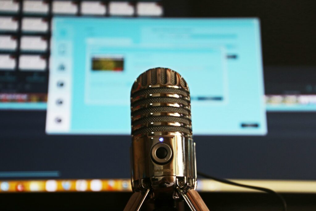 sliver old-style microphone with computer screen in the backtround. Srebrny mikrofon na pierwszym planie z ekranem komputera w tle.