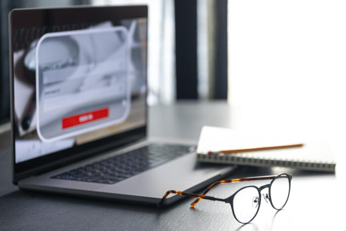 Glasses laying on the black desk and a computer and notepad with pencil in the background. Okulary leżące na czarny biurku, w tle komputer i zeszyt z ołówkiem