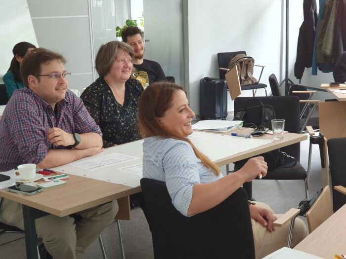Training participants sitting at the tables smiling. Uczestnicy szkolenia siedzący przy stołach i uśmiechający się.