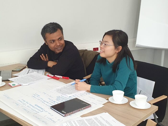 Two training participants: man from India and woman fom Japan talking at the table with notes from the training in front of them.Dwoje uczestników szkolenia: z Indii i Japonii rozmawiających przy stole z notatkami ze szkolenia.