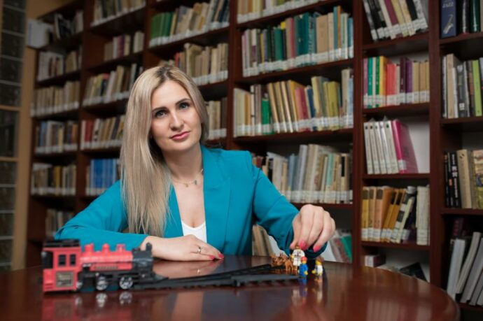 dr Mariola Paruzel-Czachura, prof. UŚ siedząca przy stole, w tle półki biblioteczne