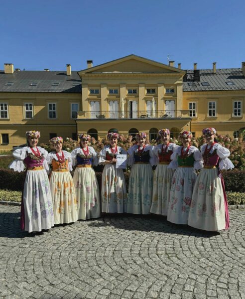Kobiety w strojach ludowych pozujące do zdjęcia na tle dworku.