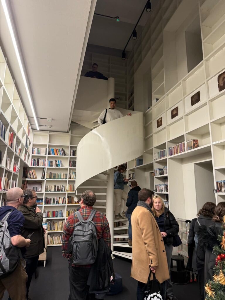 Grupa osób w bibliotece, na pierwszym planie kręte schody.