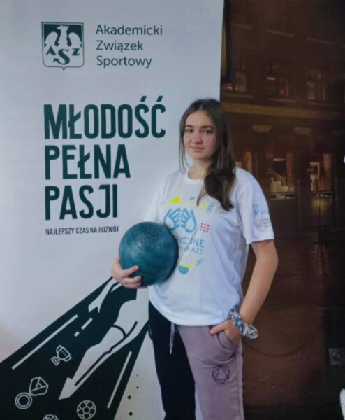 studentka w stroju sportowym z piłką w ręce, w tle baner AZS