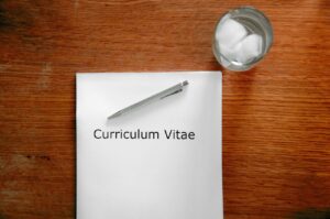 kartka z napisem „Curriculum Vitae”, długopis oraz szklanka z wodą i lodem