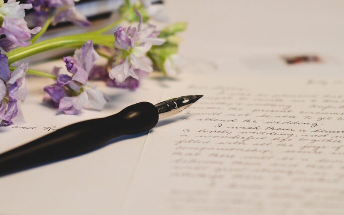 pióro, zapisana odręcznie kartka i fioletowe kwiaty