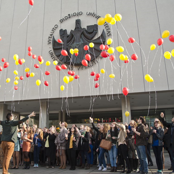 młodzi ludzie przed uczelnią wypuszczają kolorowe balony