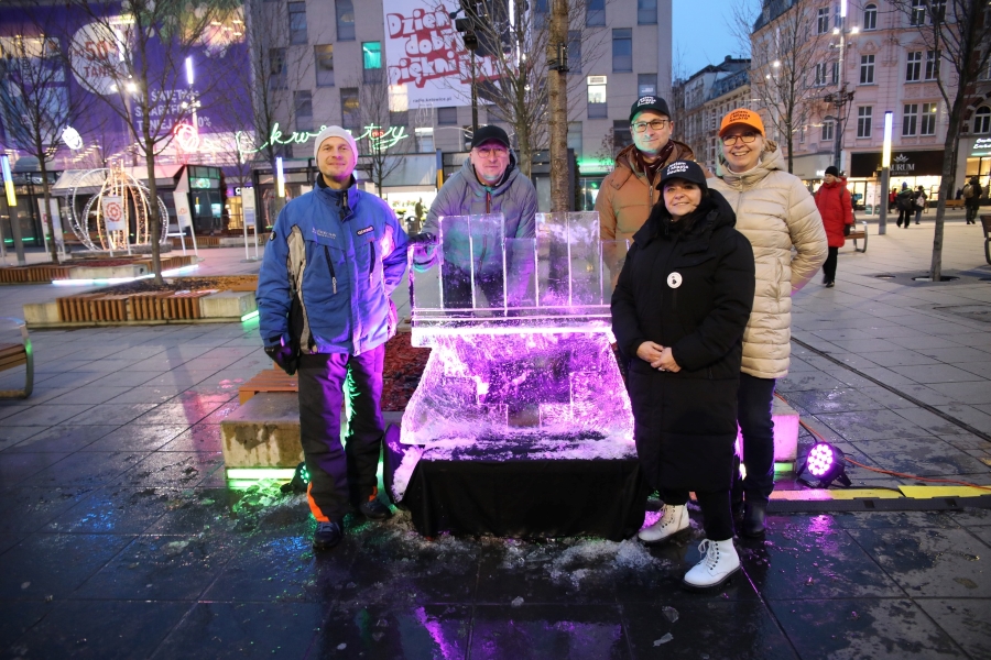 Zdjęcie przedstawia czwórkę ludzi pozujących przy lodowej rzeźbie przedstawiającej logotyp Miasta Katowice