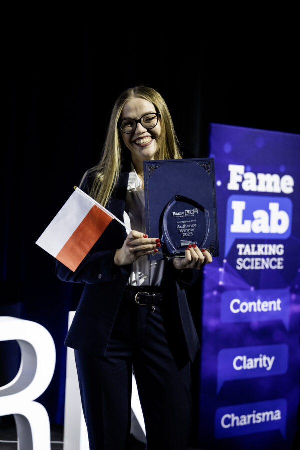 Na zdjęciu kobieta trzyma nagrodę publiczności oraz Polską flagę