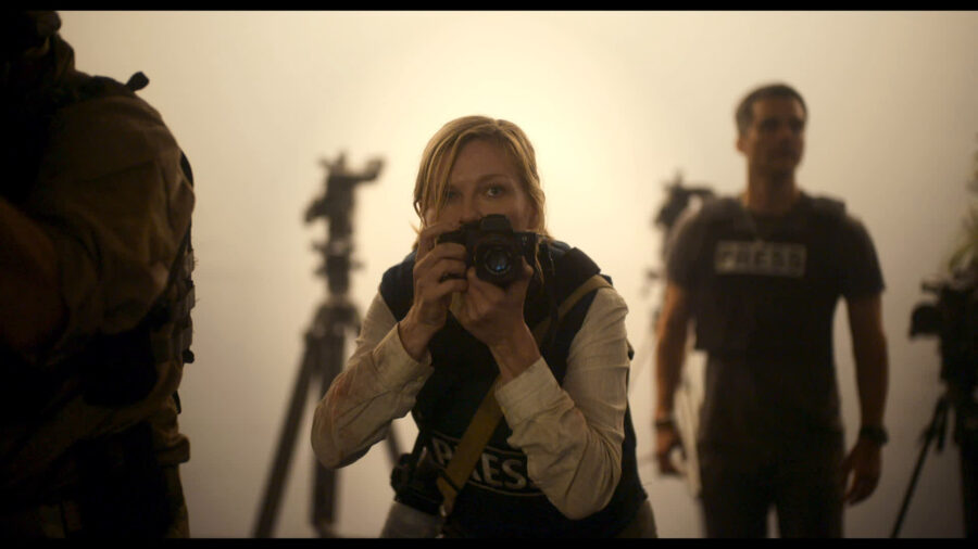 Zdjęcie przedstawia fotoreporterkę z aparatem obok niej stoją żołnierze