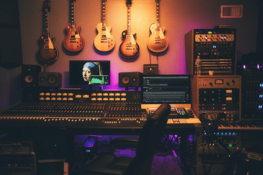 Na zdjęciu widać studio audio oraz komputer z obrazem kobiety z perłą. Na ścianie widać powieszone gitary. studio posiada masę głośników oraz komputerów