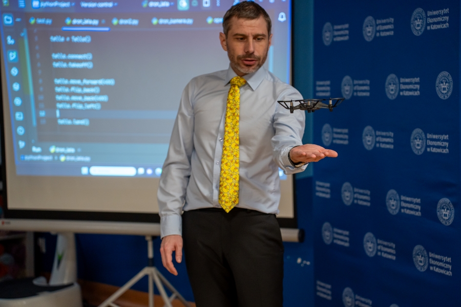 Zdjęcie przedstawia mężczyznę trzymającego otwartą dłoń. Nad dłonią unosi się mały dron