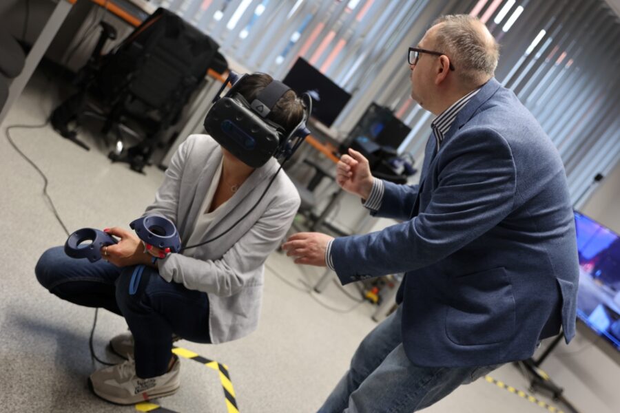 Kobieta ma założone gogle vr w rękach trzyma pady obok szkoleniowiec wyjaśnia jak działa program i urządzenie