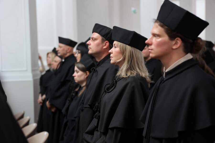 Dyplomowani doktoranci stoją do hymnu