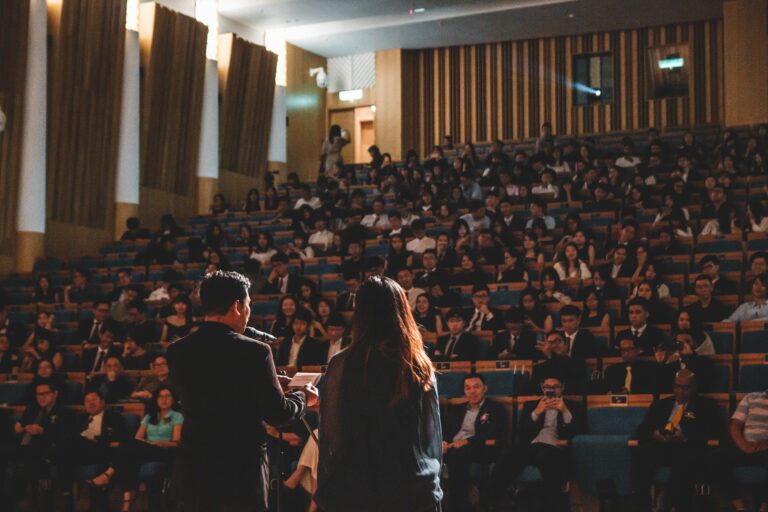 Zdjęcie przedstawia dwójkę osób na scenie przed publicznością zebraną na sali konferencyjnej