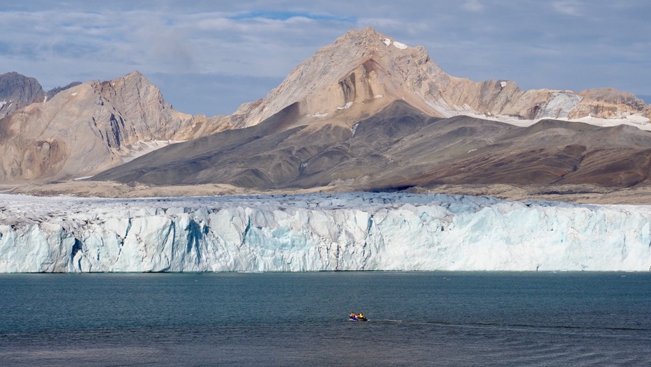 Krajobraz, szczyty w tle, kawałek odsłoniętego lodowca, morze i łódka z naukowcami