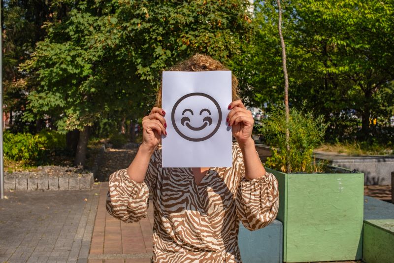 Dr Emilia Bańczyk trzyma na wysokości twarzy kartkę z uśmiechniętą emoji. Za nią widać rośliny