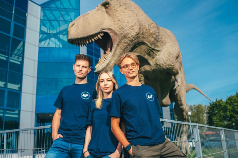 troje studentów pozuje do zdjęcia, w tle dinozaur