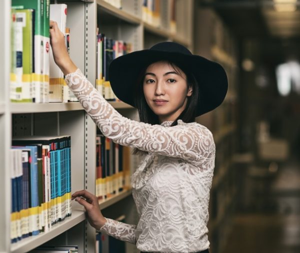 Młoda kobieta w kapeluszu stoi przy półce z książkami
