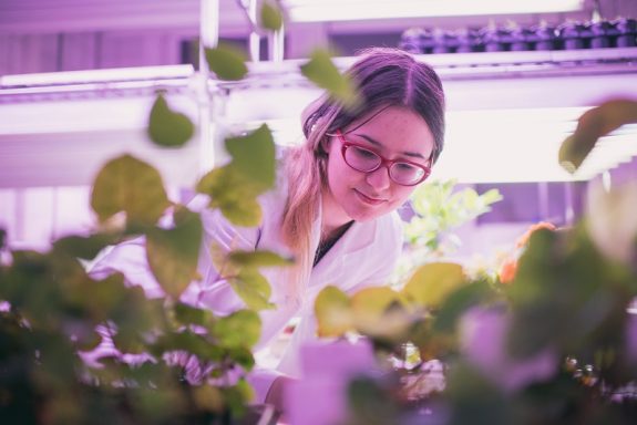 dziewczyna w laboratorium pochyla się nad roślinami/girl leaning over plants in a laboratory