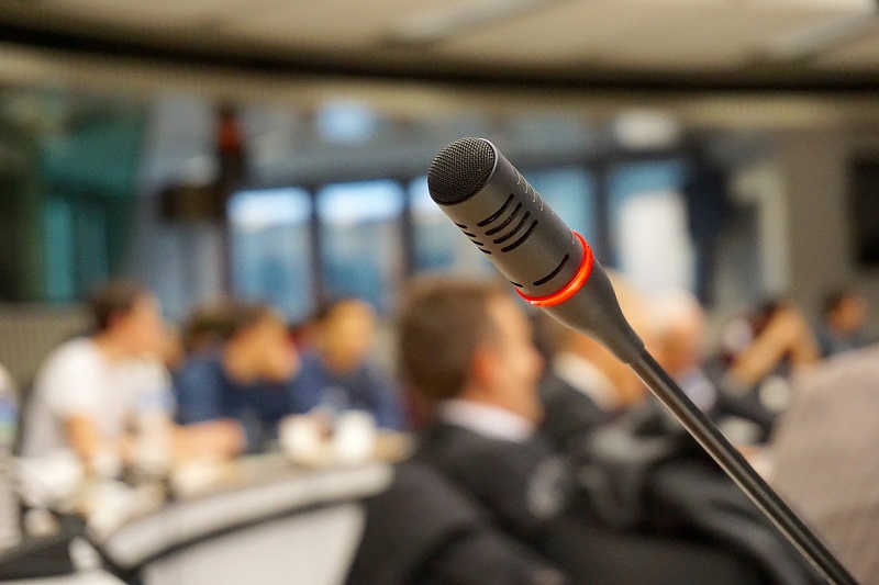 zdjęcie mikrofonu, w tle uczestnicy konferencji/photo of the microphone, conference participants in the background