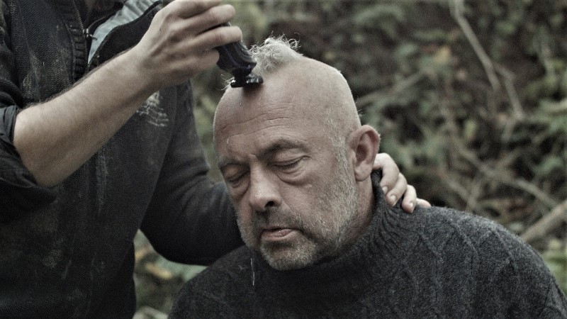 Kadr z filmu: dojrzały mężczyzna, któremu ktoś goli głowę 