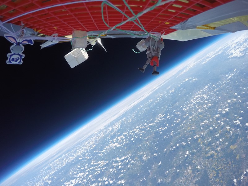 Zdjęcie zrobione w stratosferze: w tle widać Ziemię, na pierwszym planie fragment kapsuły i zawieszki dwóch robotów i Usiołka