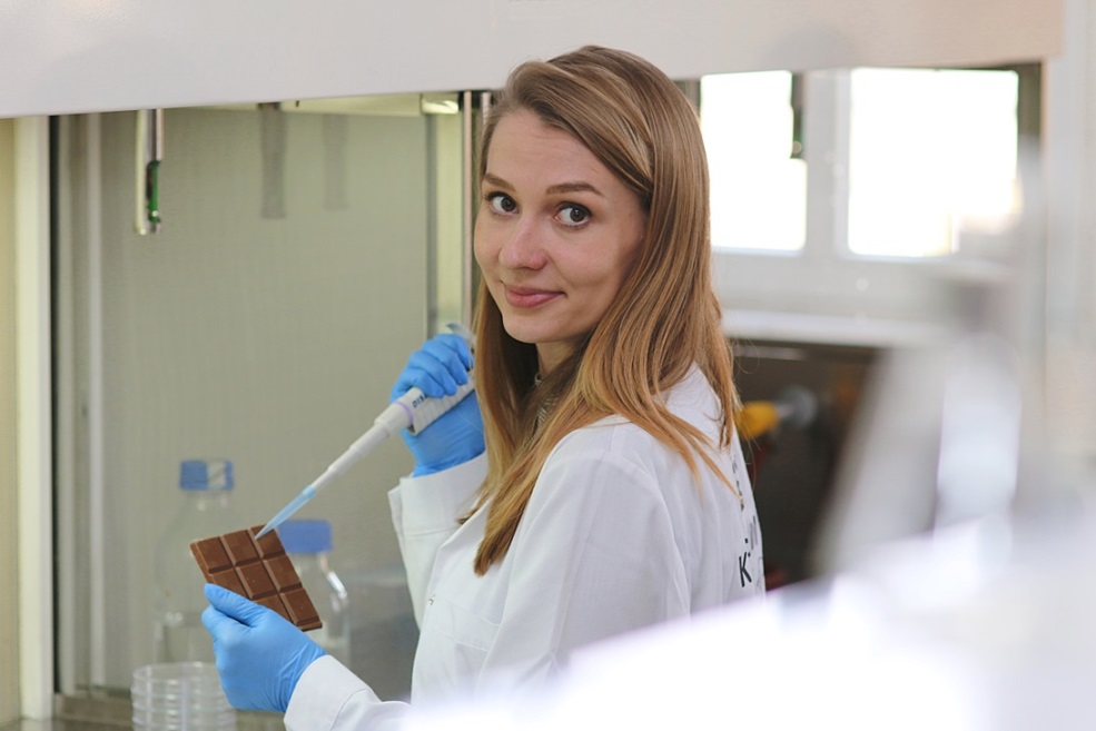 Kobieta w laboratorium, trzyma w jednej ręce czekoladę, w drugiej pipetę