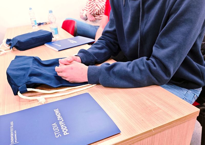 dyplom studiów podyplomowych na biurku i osoba siedząca