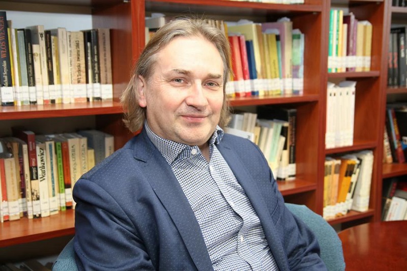 Dr hab. Dariusz Szostek, prof. UŚ siedzi na fotelu, za nim regał z książkami/ Dariusz Szostek, PhD, DLitt, Associate Professor, sitting in a chair with book shelves behind him