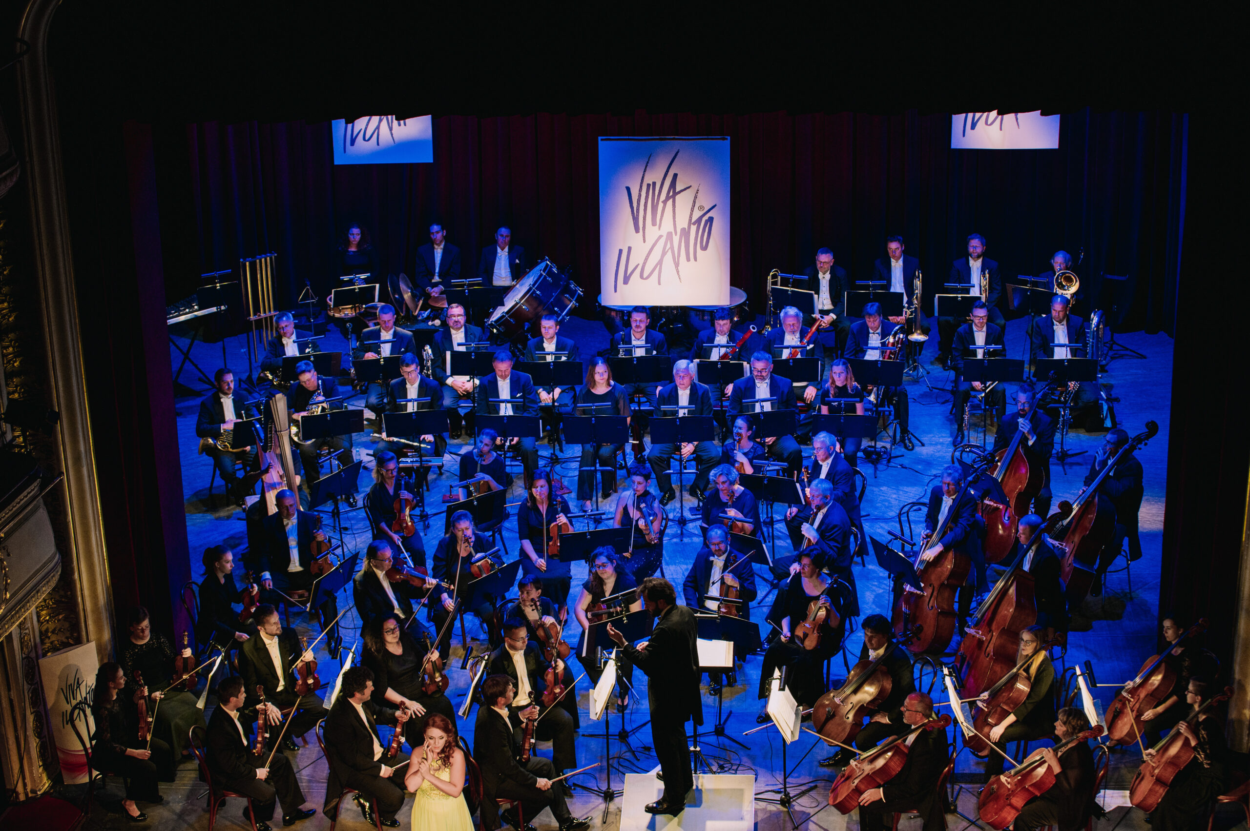 Scena koncertowa wypełniona artystami grającymi na różnych instrumentach. W tle trzy ekrany wyświetlające nazwę festiwalu