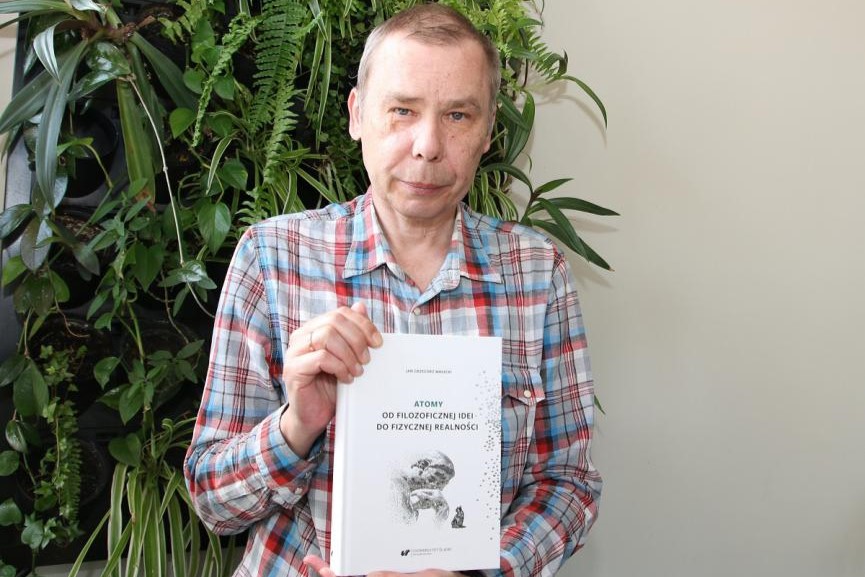 Prof. dr hab. Jan Małecki pozuje do zdjęcia trzymając w dłoniach swoją książkę