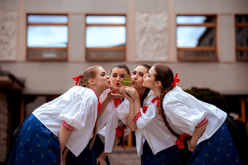Cztery dziewczyny w tradycyjnych strojach regionalnych pochylają się, by pocałować statuetkę trzymaną przez jedną z nich
